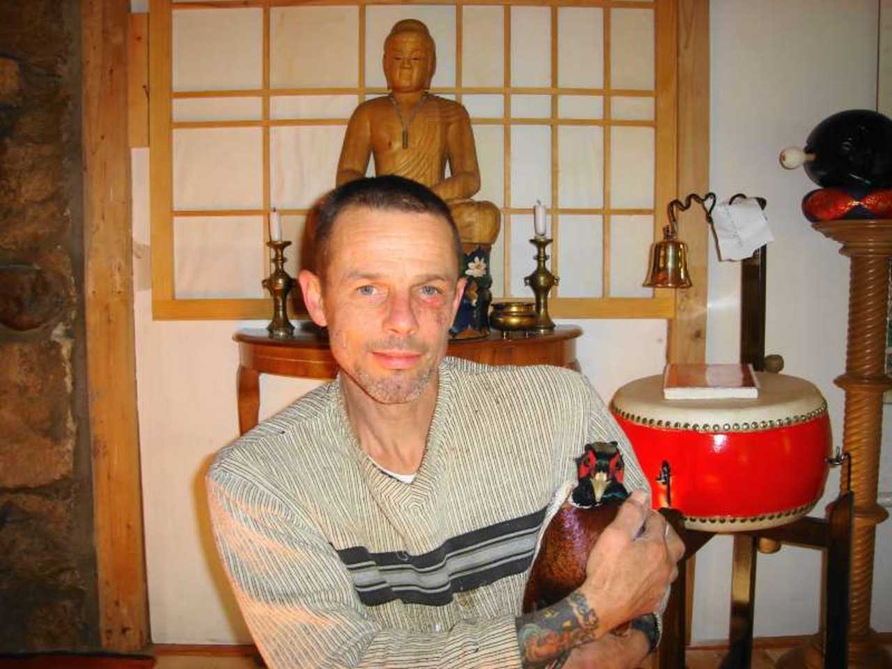 Eric Johns, holding a pheasant, in front of a Buddha statue and ceremonial drum
